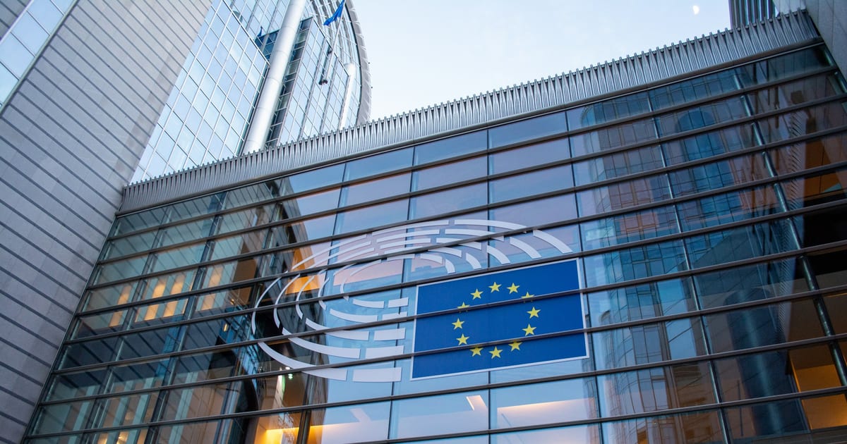 The European Union flag reflected in the glass facade of a modern building.