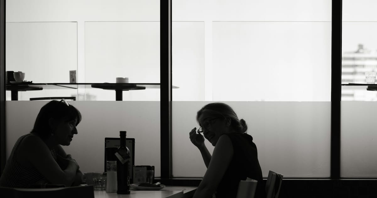 Two people in silhouette facing each other across a table in a brightly lit room.