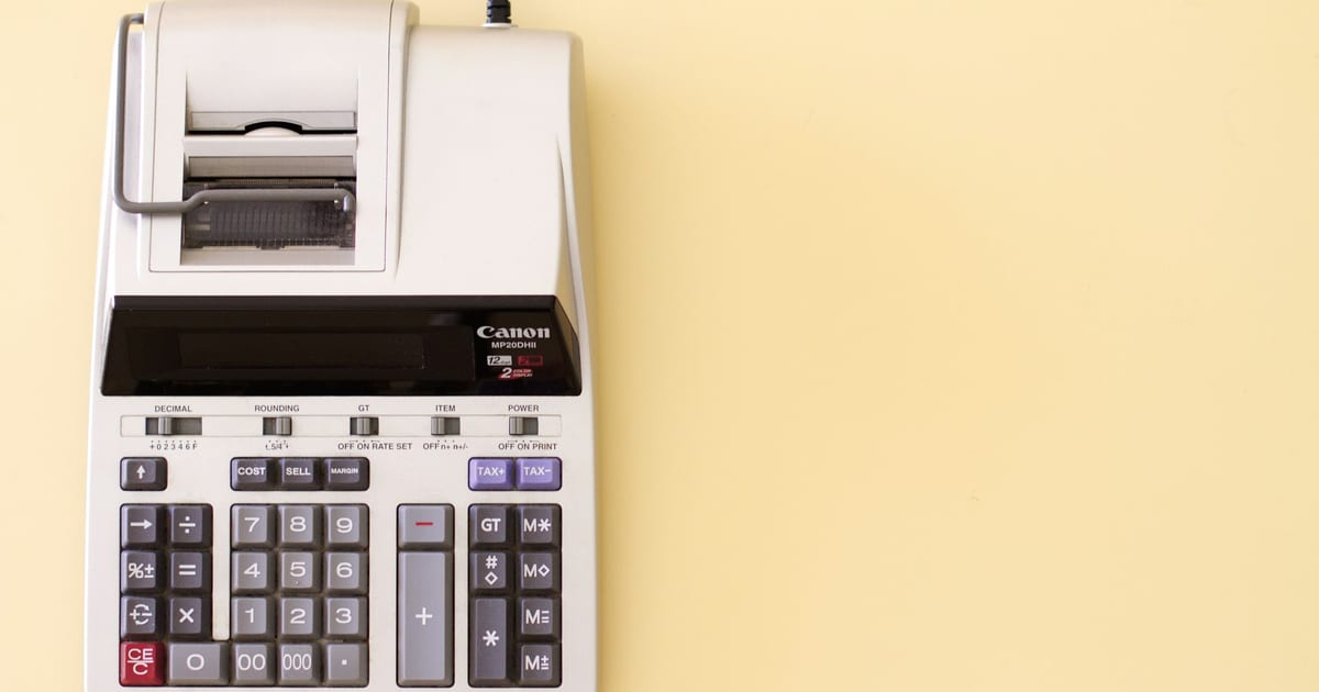 A printing calculator on a pale yellow surface, its paper roll empty.