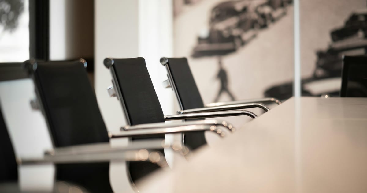A row of empty black office chairs pulled up to a long conference table.
