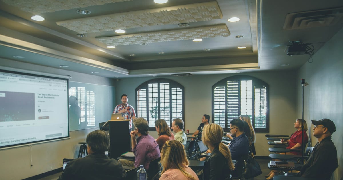 A room of people seated in rows facing a projector screen during a training session.