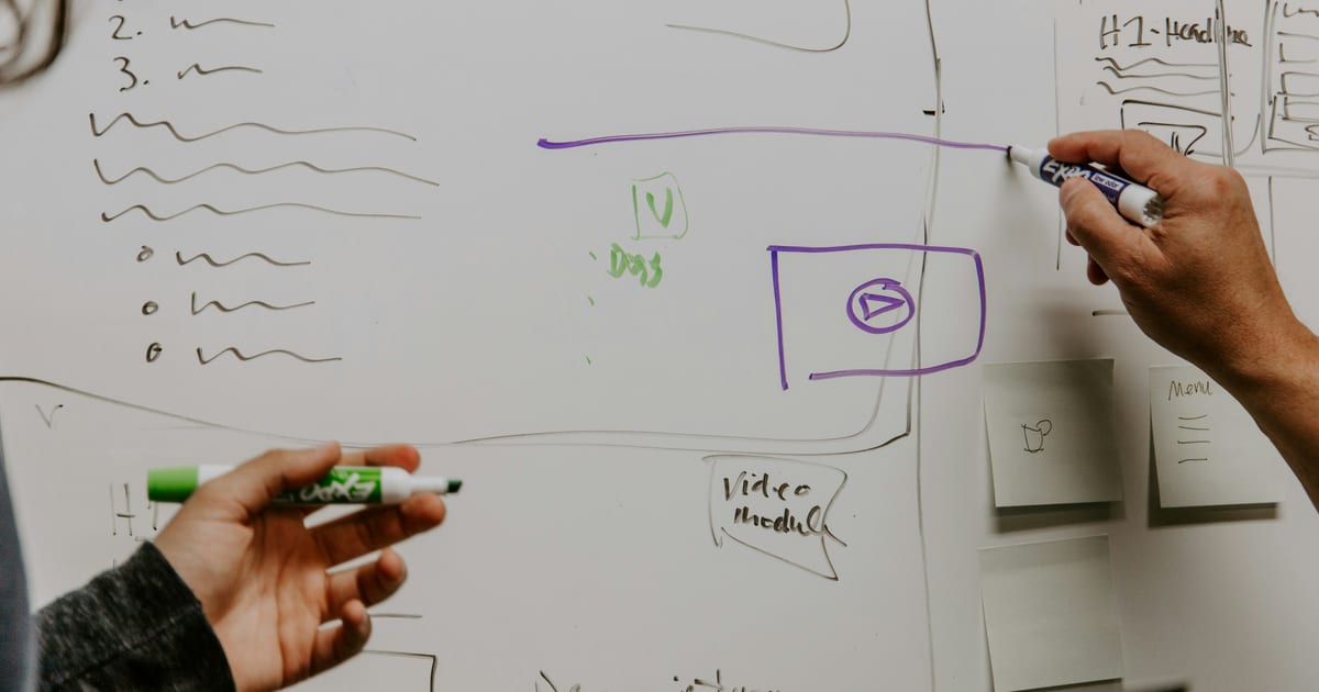 Two people standing at a whiteboard, one drawing while the other watches.
