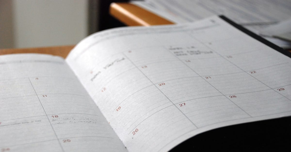 An open monthly paper planner lying on a wooden desk.