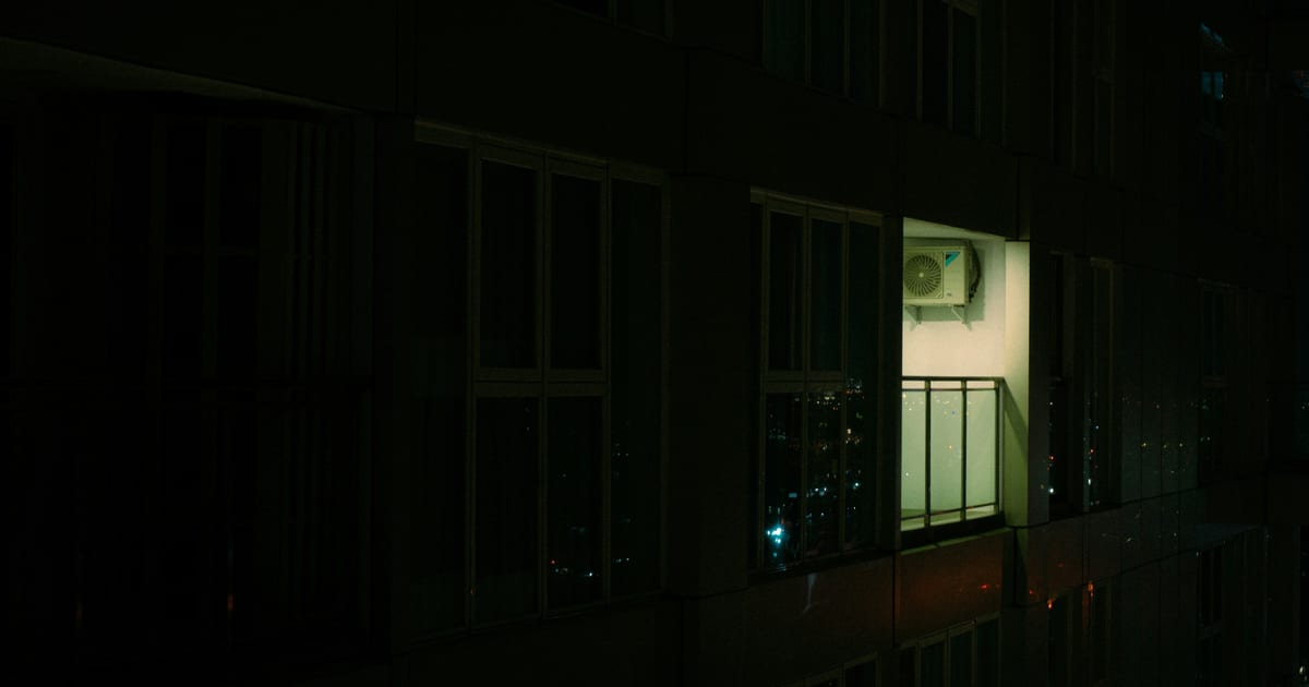 A single lit window in an otherwise dark apartment building at night.