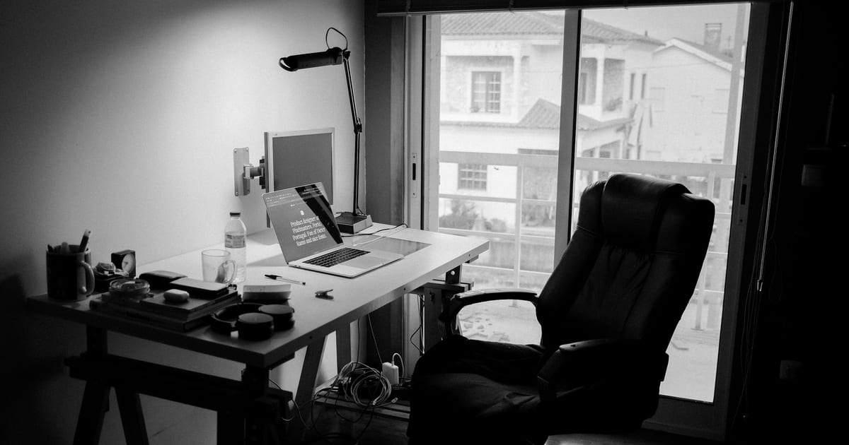 An empty office chair pushed up to a bare wooden desk.